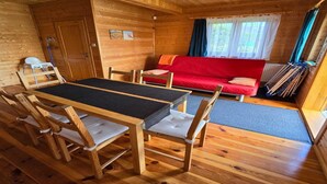A cozy cabin with a wooden interior, a dining table with chairs, a red sofa, and a window with curtains. - Terraced Home in Sarbinowo Near the Beach (Mielno)
