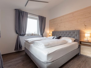 A neatly made bed with white linens, a grey headboard, and a bedside table with a lamp.