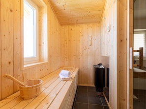 A wooden sauna with a bench, a wooden bucket, and a sauna heater.