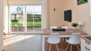 Un'elegante zona pranzo con un tavolo grande, sedie bianche e vista su un paesaggio verde attraverso ampie porte scorrevoli in vetro.