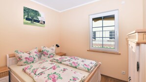 Camera da letto con un letto, biancheria da letto floreale, una finestra vista, un comodino e una lampada a parete.