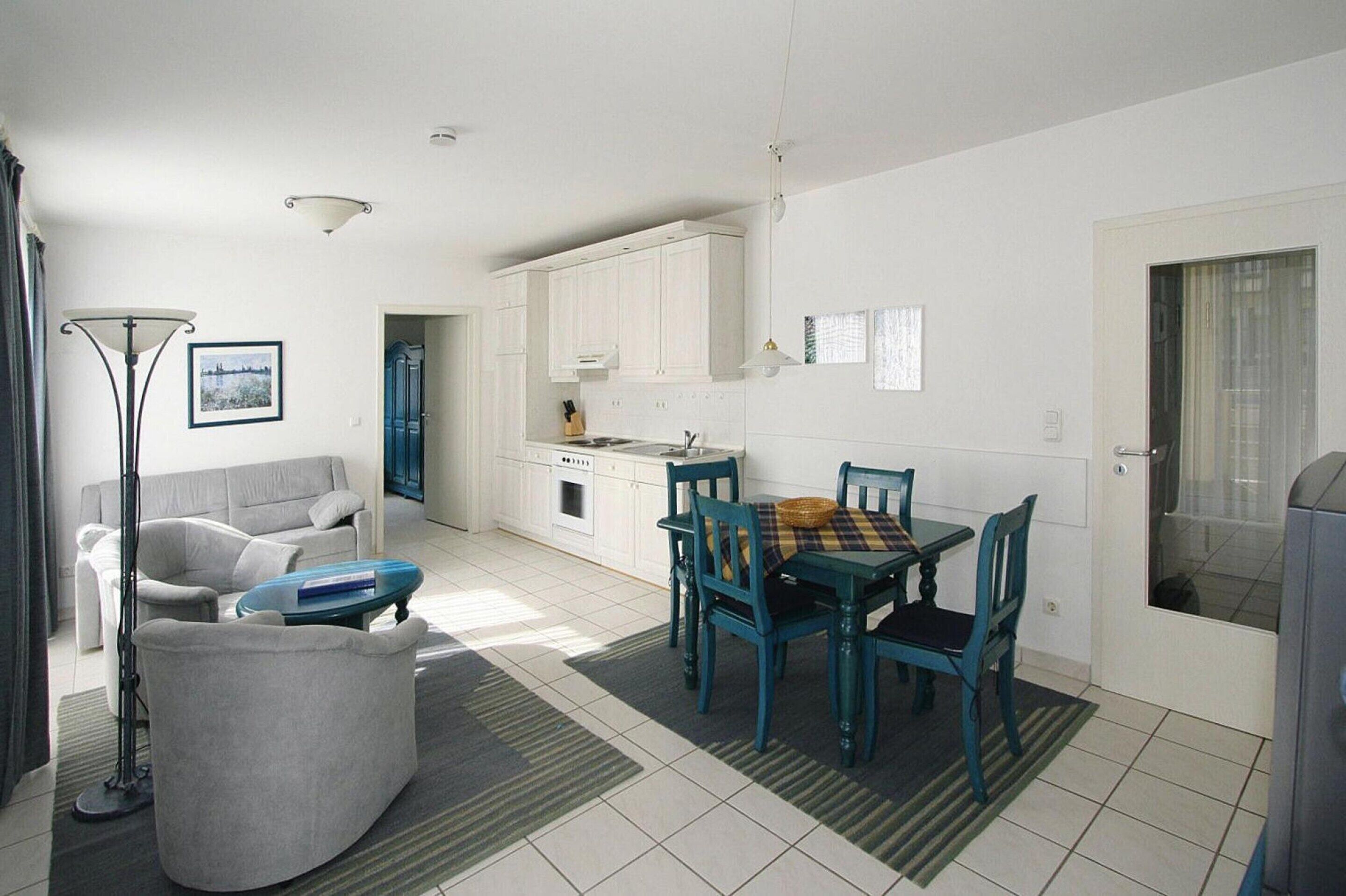 A modern kitchen with white cabinets, a dining table with chairs, a sofa, and a floor lamp.