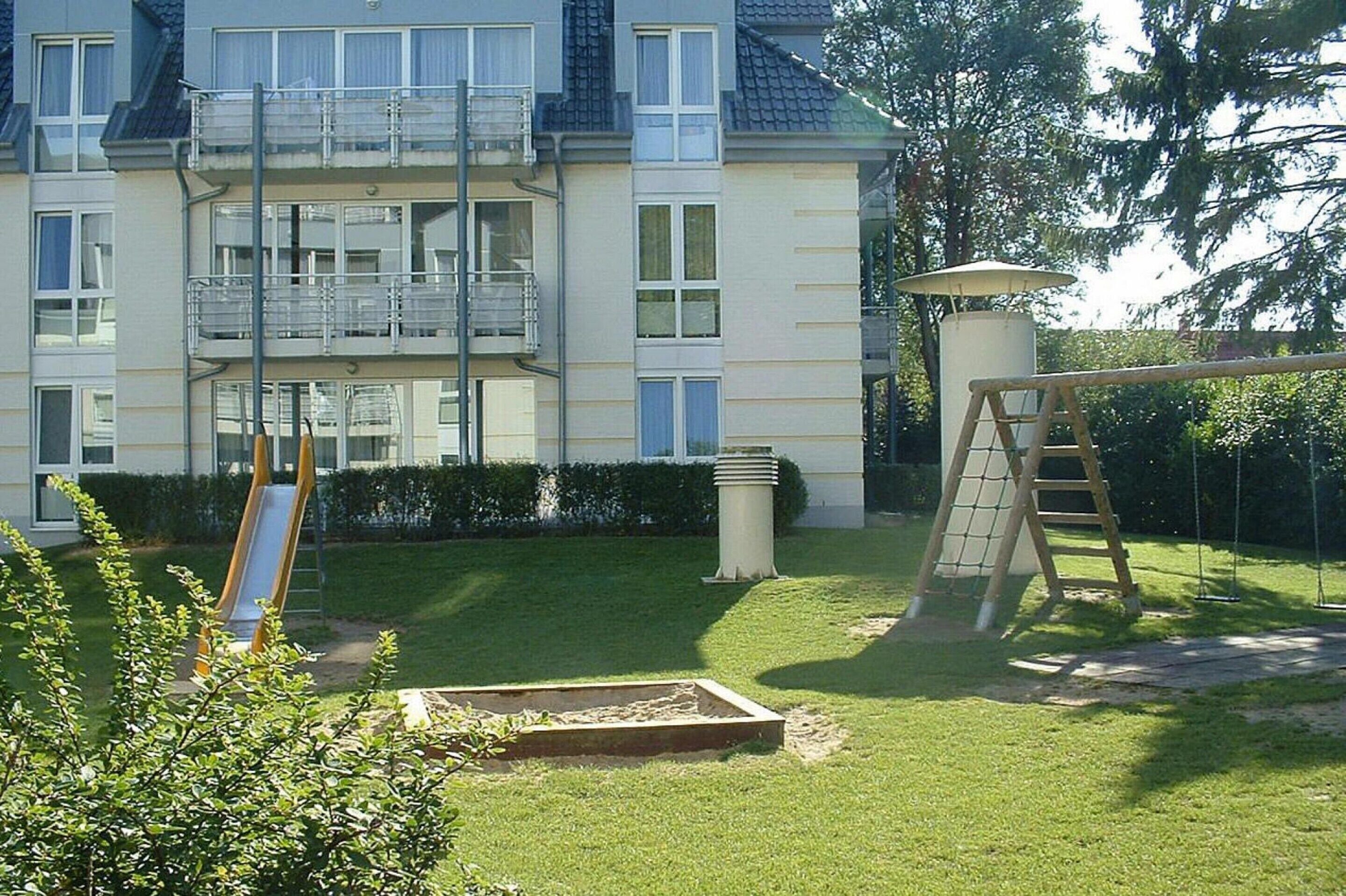 Een woongebouw met een balkon, een glijbaan en een schommel in de voortuin.