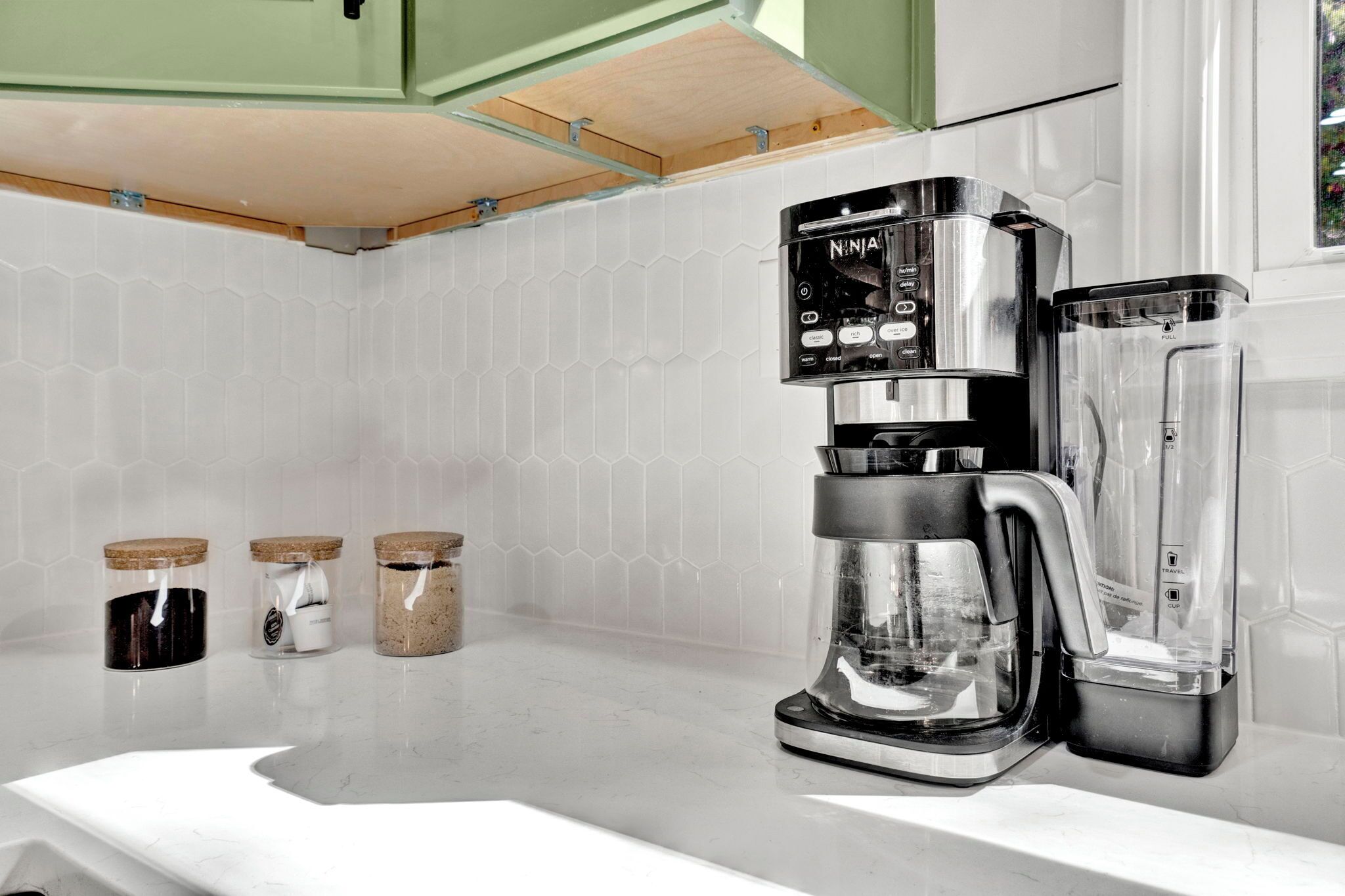 A kitchen with a coffee maker, a blender, and three jars on the counter.