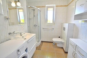 A modern bathroom with a shower, toilet, sink, and a washing machine.