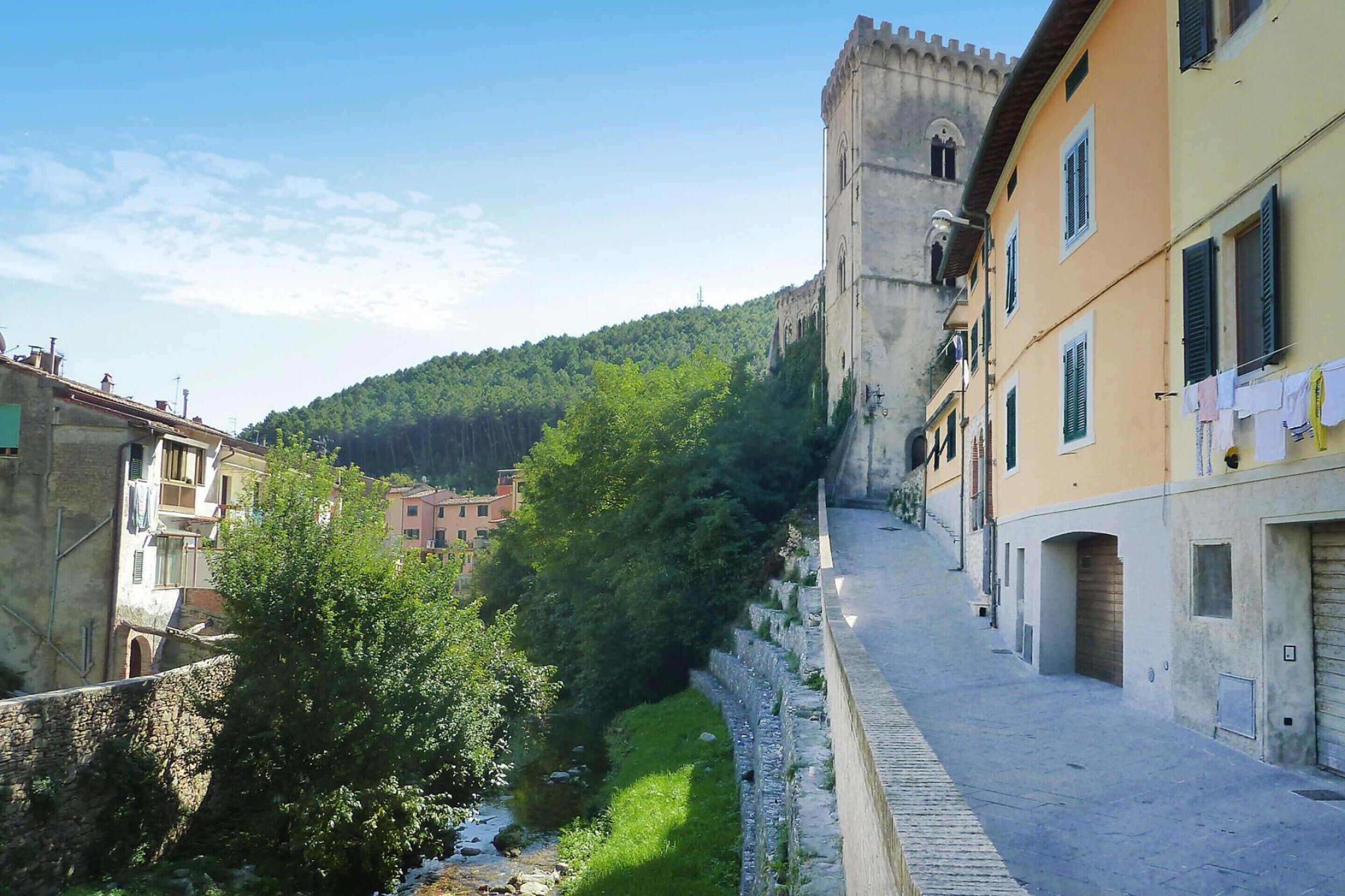 A narrow street with buildings on either side, a stone wall, and a hill in the background.