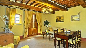 A dining area with a wooden table and chairs, yellow curtains, and a chandelier. - Estate in Monte Serra With Pool & Olive Views (Buti)