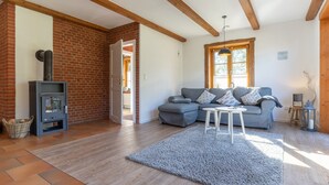 Una sala de estar con pared de ladrillo, un sofá gris, una mesa de centro blanca y una estufa de leña.