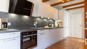 Una cocina moderna con armarios blancos, horno empotrado, cafetera y pared de ladrillo.