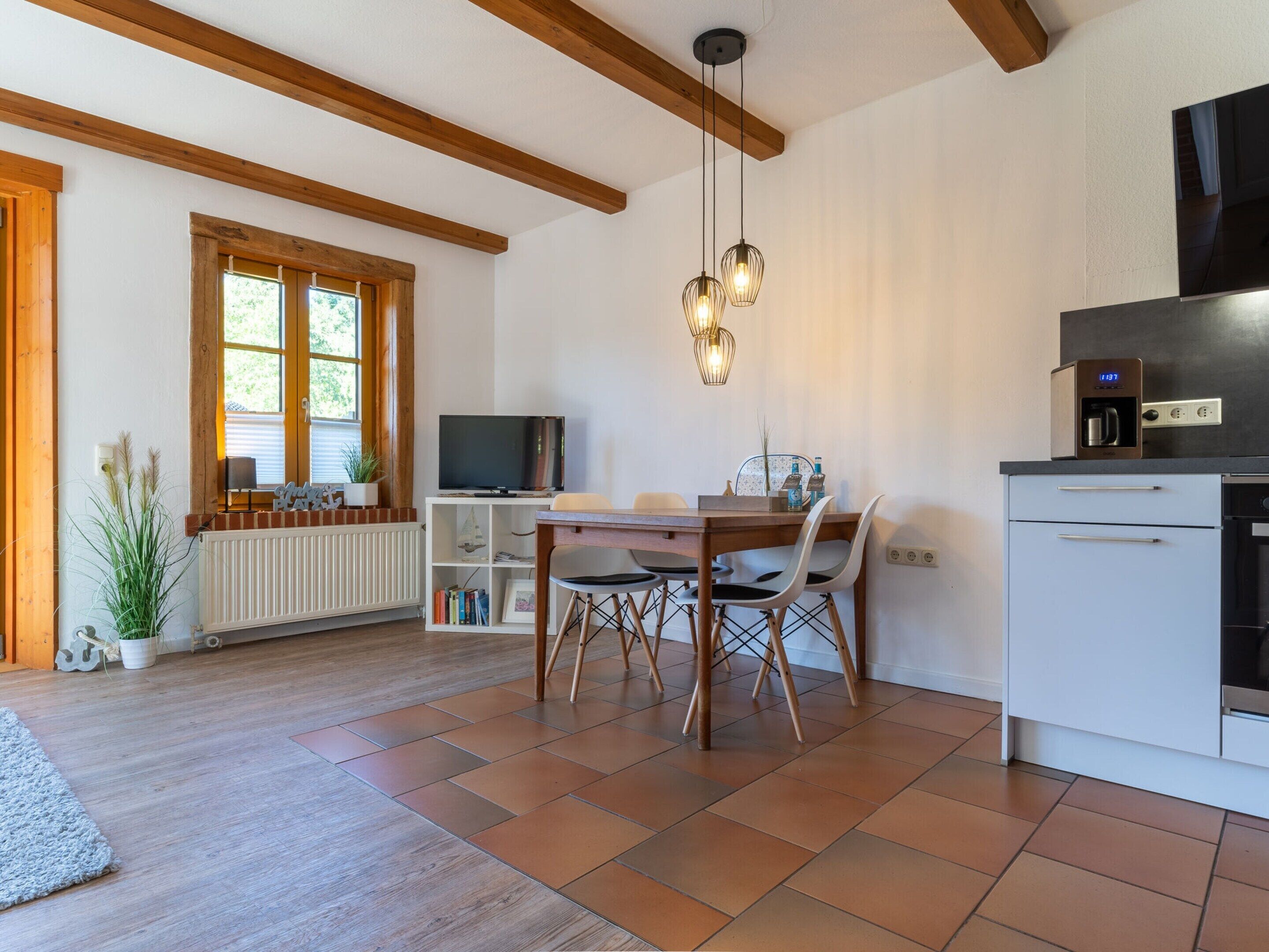 A modern kitchen with a dining area, wooden beams, a TV, and a coffee machine.