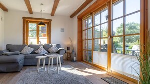 Una sala de estar acogedora con un sofá gris, una mesita blanca y un gran ventanal con persianas.