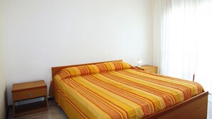 A single bed with a striped bedspread, a wooden nightstand, and a bedside table with a lamp. - Residence Ambassador, Lido del Sole (San Michele al Tagliamento)
