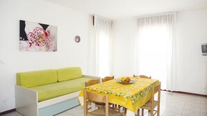 A dining area with a table set for two, a green sofa, and a wall-mounted painting. - Residence Ambassador, Lido del Sole (San Michele al Tagliamento)