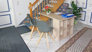 Une pièce avec un escalier en bois, un bureau avec des chaises, un vase de fleurs et un tapis à motifs.