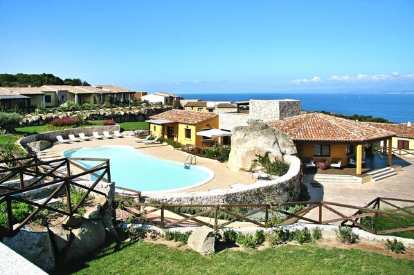 A resort with a swimming pool, multiple buildings with terracotta roofs, and a view of the sea. - Holiday Residence Punta Falcone (Santa Teresa di Gallura)