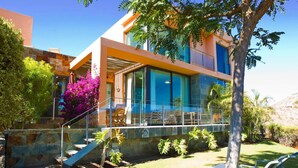 A modern house with a glass balcony, a stone staircase, and a well-maintained lawn. - Holiday Home, Maspalomas (San Bartolomé de Tirajana)