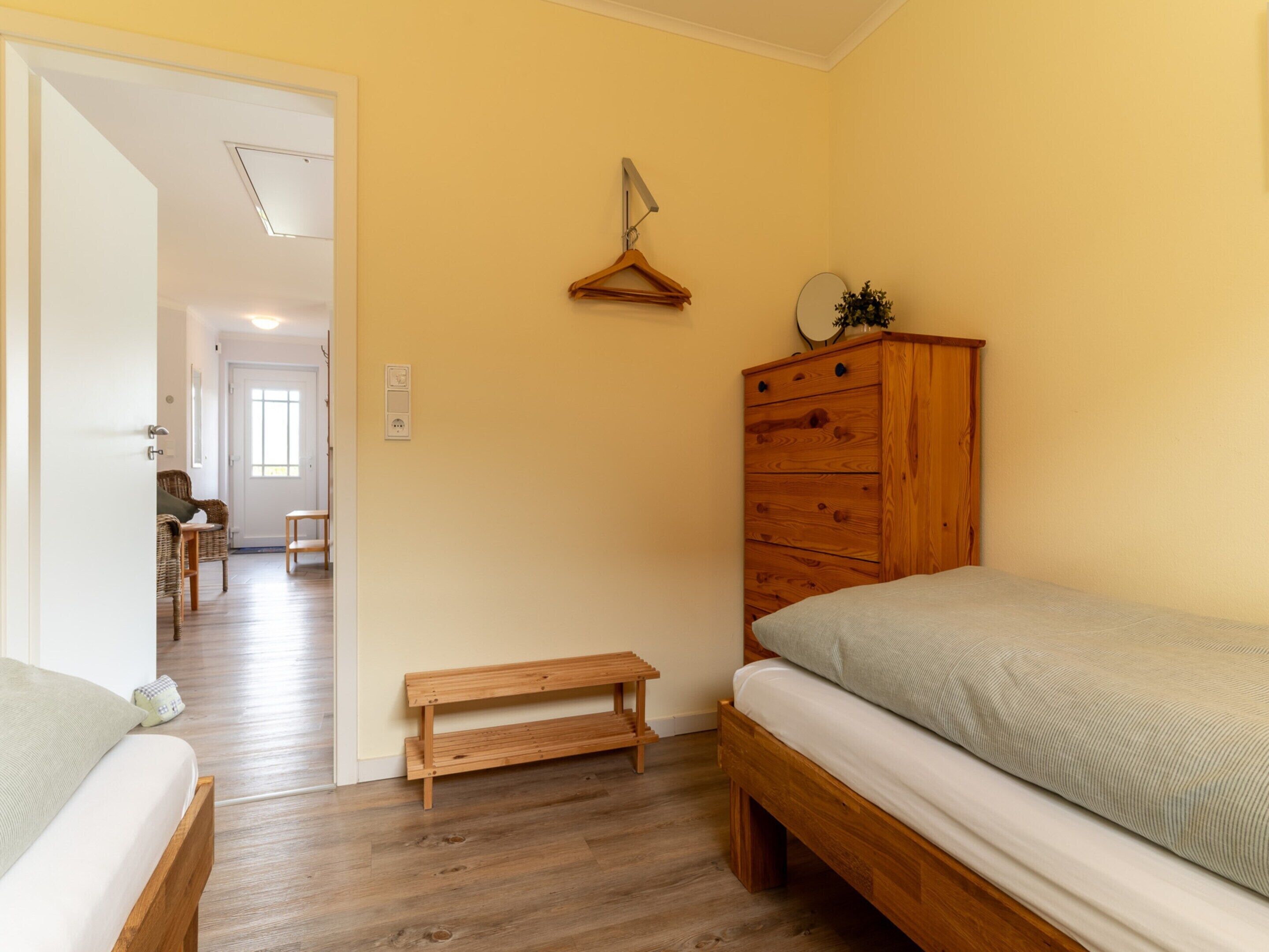 Une chambre avec un lit en bois, une commode en bois, un banc et un miroir accroché au mur.