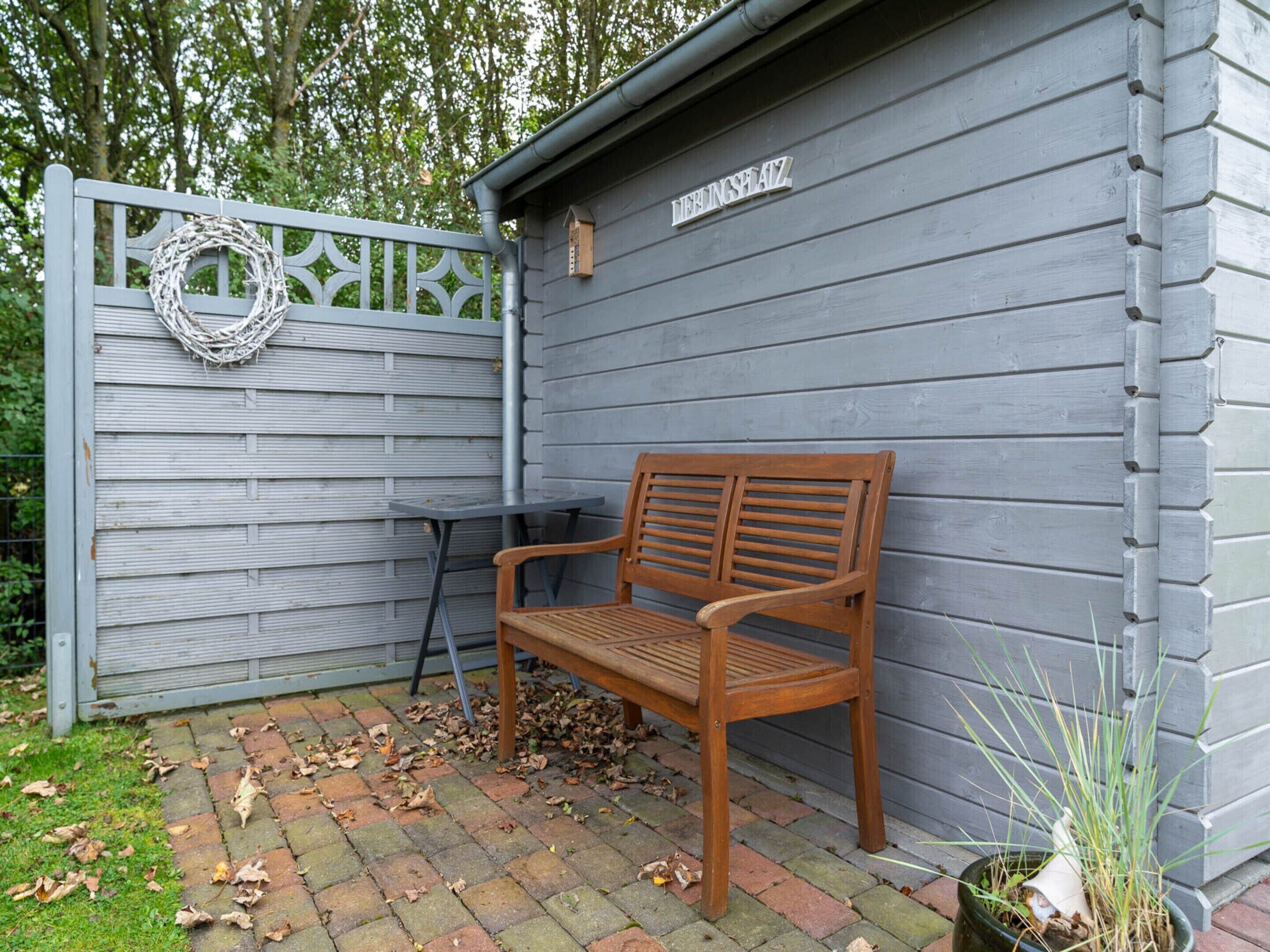 A wooden bench outside a building with a grey exterior and a metal gate.