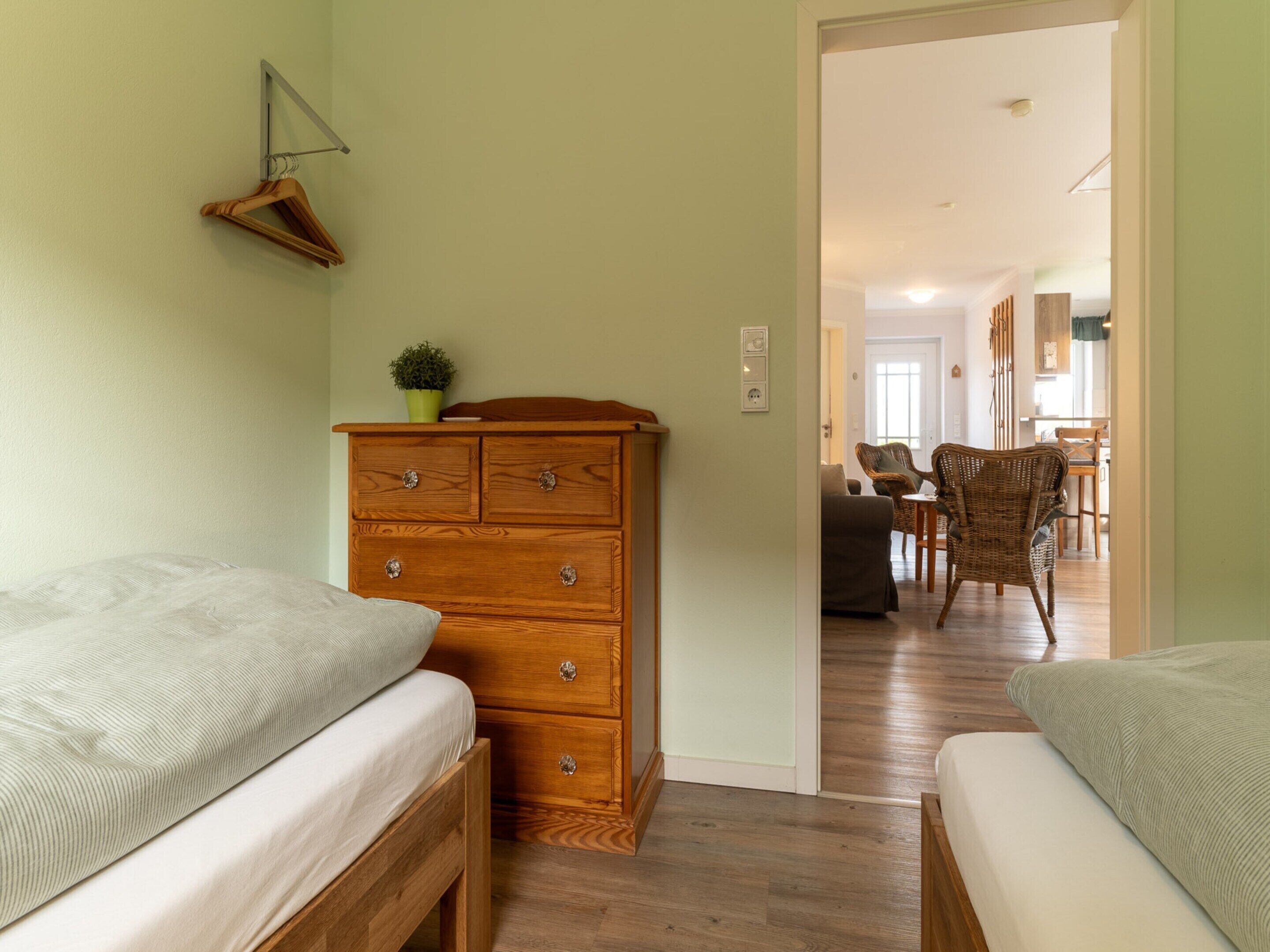 Een slaapkamer met twee bedden, een houten dressoir en een gang die uitkomt in een eetruimte.