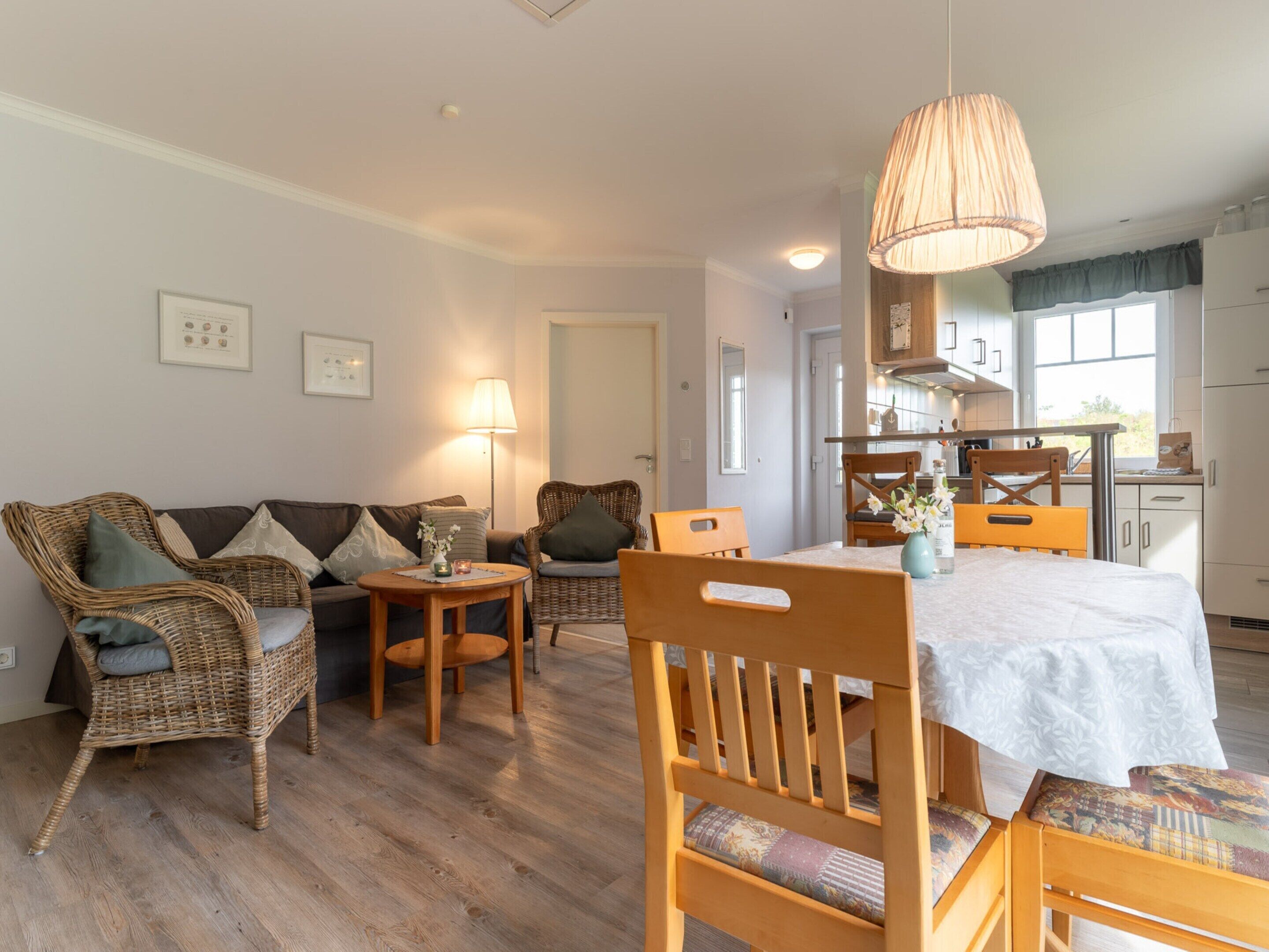 Un salon chaleureux avec un canapé, des fauteuils, une table à manger et une cuisine en arrière-plan.