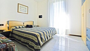 Une chambre d’hôtel comprenant un lit, une table de chevet, une lampe, une armoire et une fenêtre avec des rideaux.