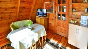 A cozy wooden cabin interior with a dining table, a television, and a kitchen area. - Comfortable Holiday Home Near Lake Jamno (gmina Sianów)