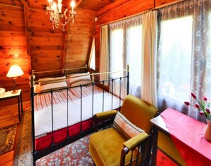 A wooden cabin bedroom with a bed, a chair, a table, and a chandelier. - Comfortable Holiday Home Near Lake Jamno (gmina Sianów)