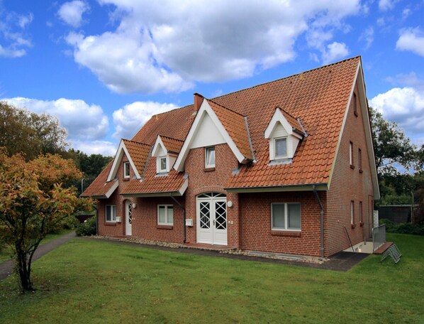 A two-story brick house with a red-tiled roof, a front porch, and a well-maintained lawn. - Ferienwohnung in St. Peter-ording (St. Peter-Ording)