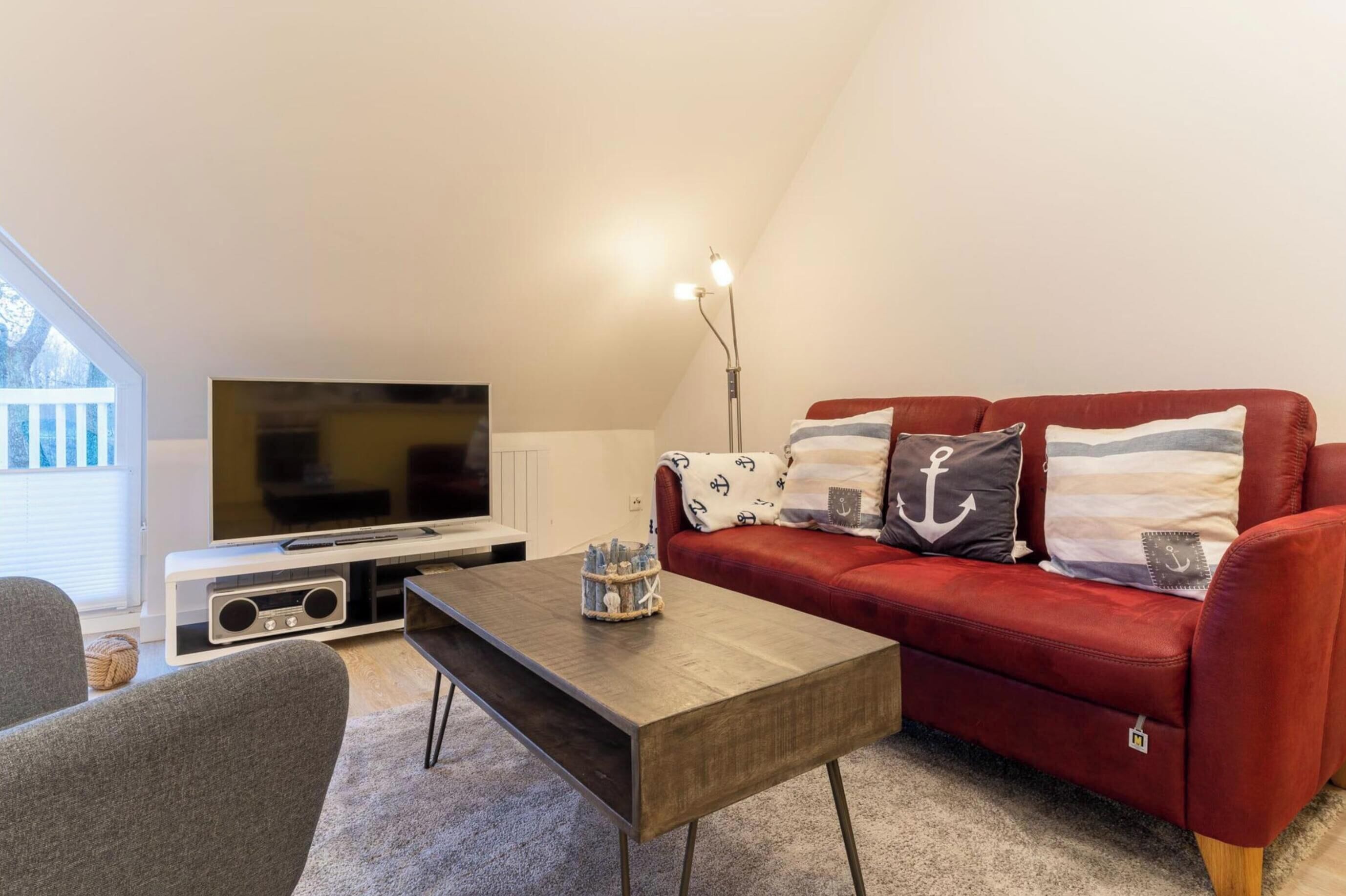 A living room with a red sofa, a television, a coffee table, and a lamp.