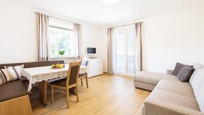 A modern living room with a sofa, a dining table with chairs, a TV, and a balcony with curtains. - Apartment in Dorf Tirol Near Spronser Lakes (Tirolo)