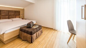 A modern hotel room with a large bed, a wooden headboard, a small bedside table, a chair, and a window with sheer curtains. - Apartment in Dorf Tirol Near Spronser Lakes (Tirolo)