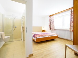A bedroom with a bed, a bedside table, a window with curtains, a radiator, and a shower area. - Apartment in Dorf Tirol Near Spronser Lakes (Tirolo)