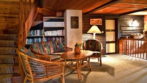 A cozy room with a wooden staircase, a sofa, a chair, a table, and a bookshelf filled with books. - Farmhouse in Afritz Near Gerlitzen Ski Center (Treffen)