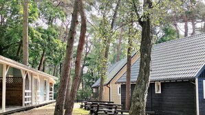 A rustic cabin with a wooden exterior, surrounded by tall trees and a picnic area with benches. - Cottage in Pobierowo for 5 People (Rewal)