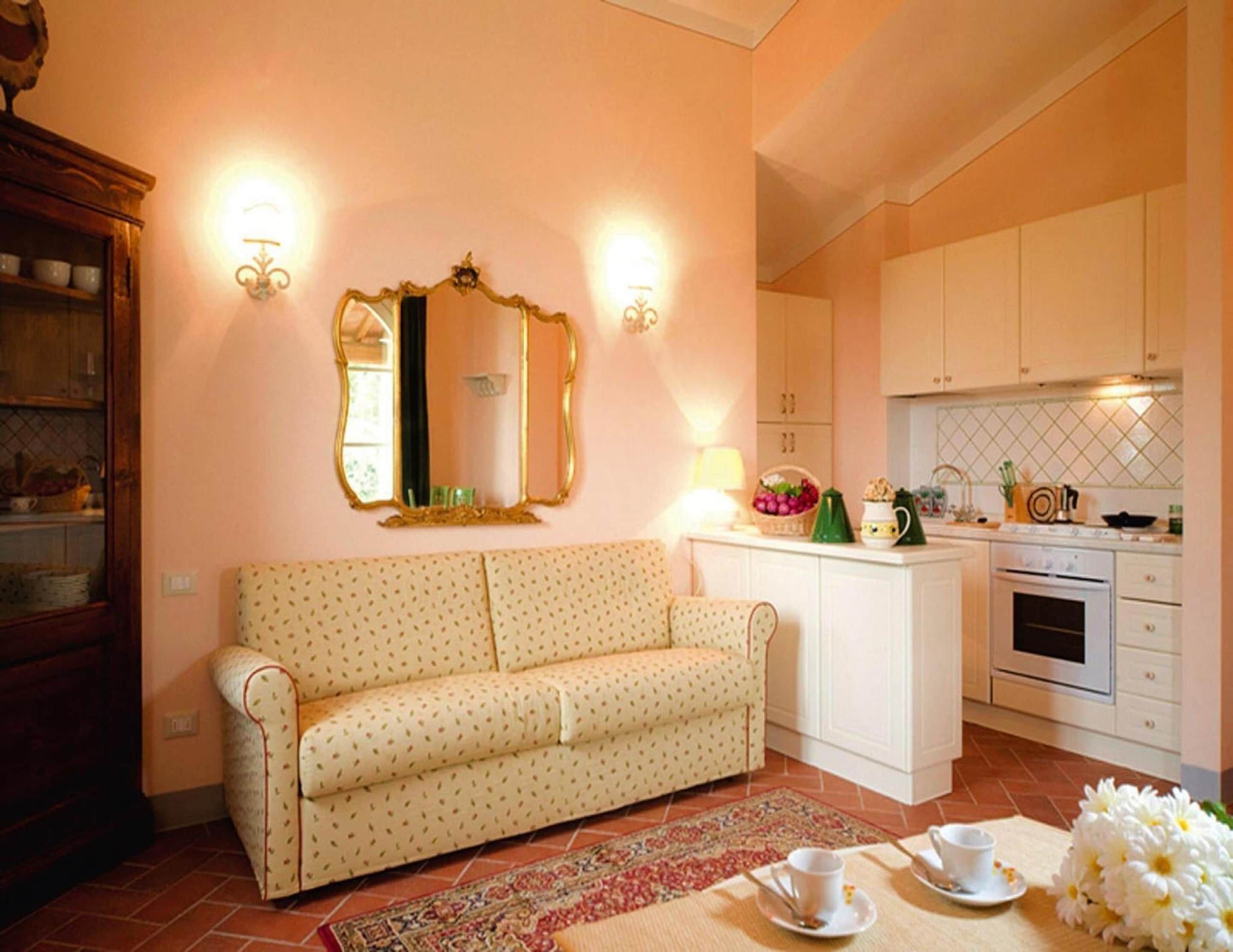 A cozy living room with a sofa, a dining area with a table set for two, and a kitchen with white cabinets and a stove.