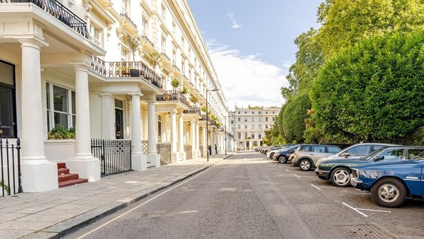 A row of white buildings with balconies, parked cars, and a clear sky. - London Oasis Retreat - 2 Bedroom Apartment (London)