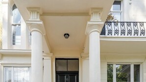 A building entrance with a black door, white columns, and a red staircase leading up to the door. - London Oasis Retreat - 2 Bedroom Apartment (London)