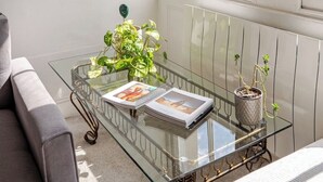 A room with a glass coffee table, a grey sofa, a window with blinds, and a radiator. - London Oasis Retreat - 2 Bedroom Apartment (London)