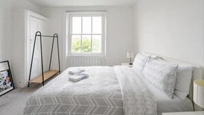 A bedroom with a bed, a window, a radiator, a ladder, and a framed picture on the floor. - London Oasis Retreat - 2 Bedroom Apartment (London)