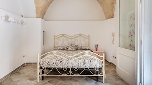 A bedroom with a bed, a nightstand, a phone, and a door with a floral curtain. - Terra Mia In The Historic Center Of Lecce (Lecce)