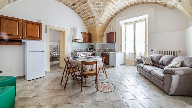 A spacious kitchen with a stone ceiling, wooden cabinets, a dining table with chairs, and a grey sofa. - Terra Mia In The Historic Center Of Lecce (Lecce)