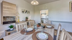 A dining area with a wooden table set for four, surrounded by chairs, and a kitchen in the background. - Pool House Lilly in Vi Njan (Visnjan)