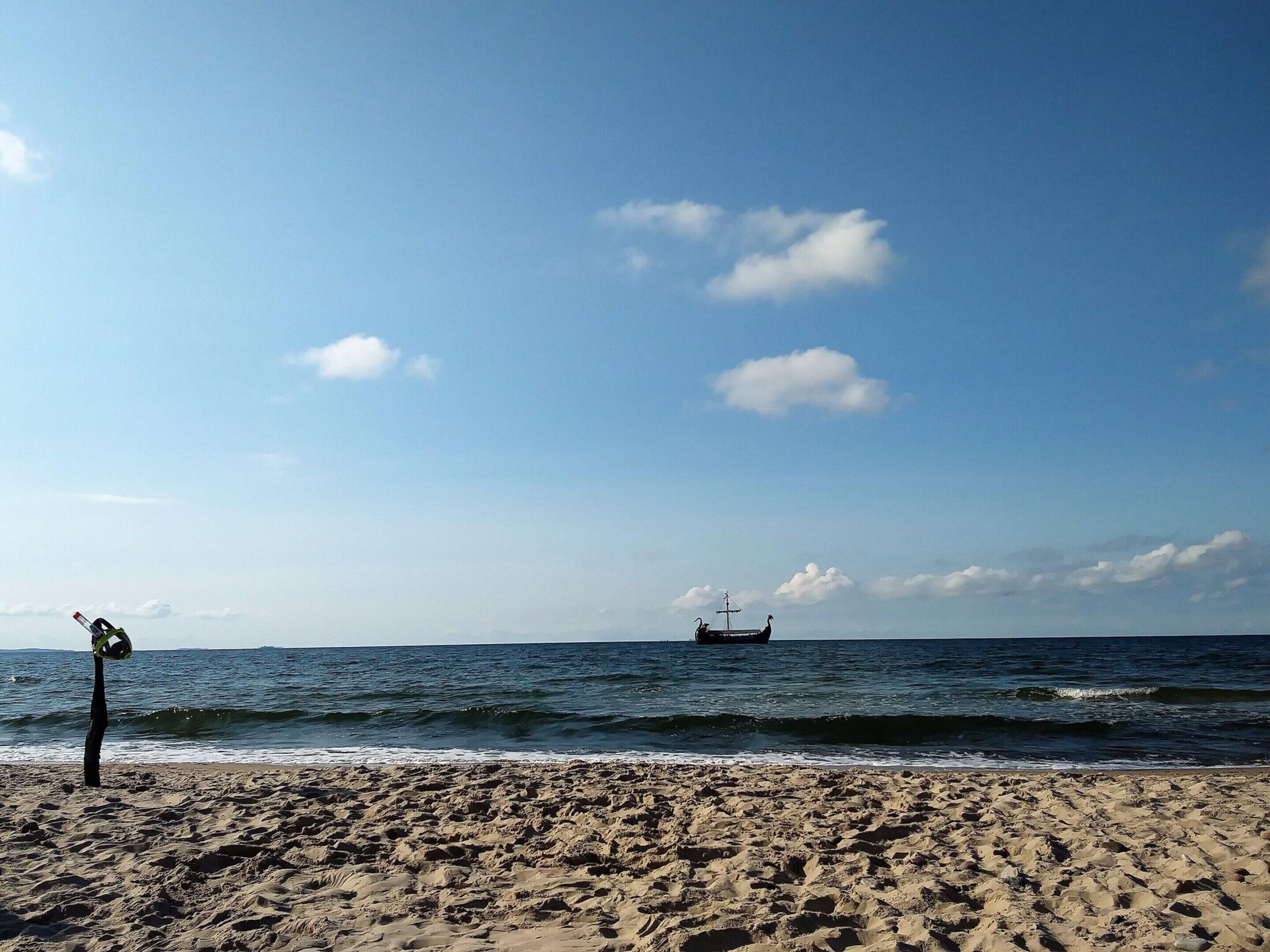 A beach with a ship in the distance and a windmill on the left.