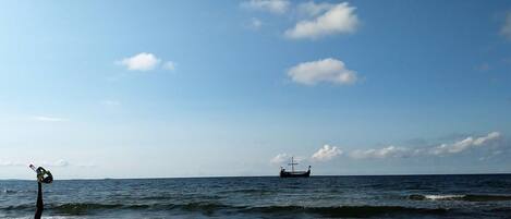 A beach with a ship in the distance and a windmill on the left.