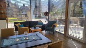 En moderne stue med en sort lædersofa, en grøn lænestol og et spisebord med krystalglas.
