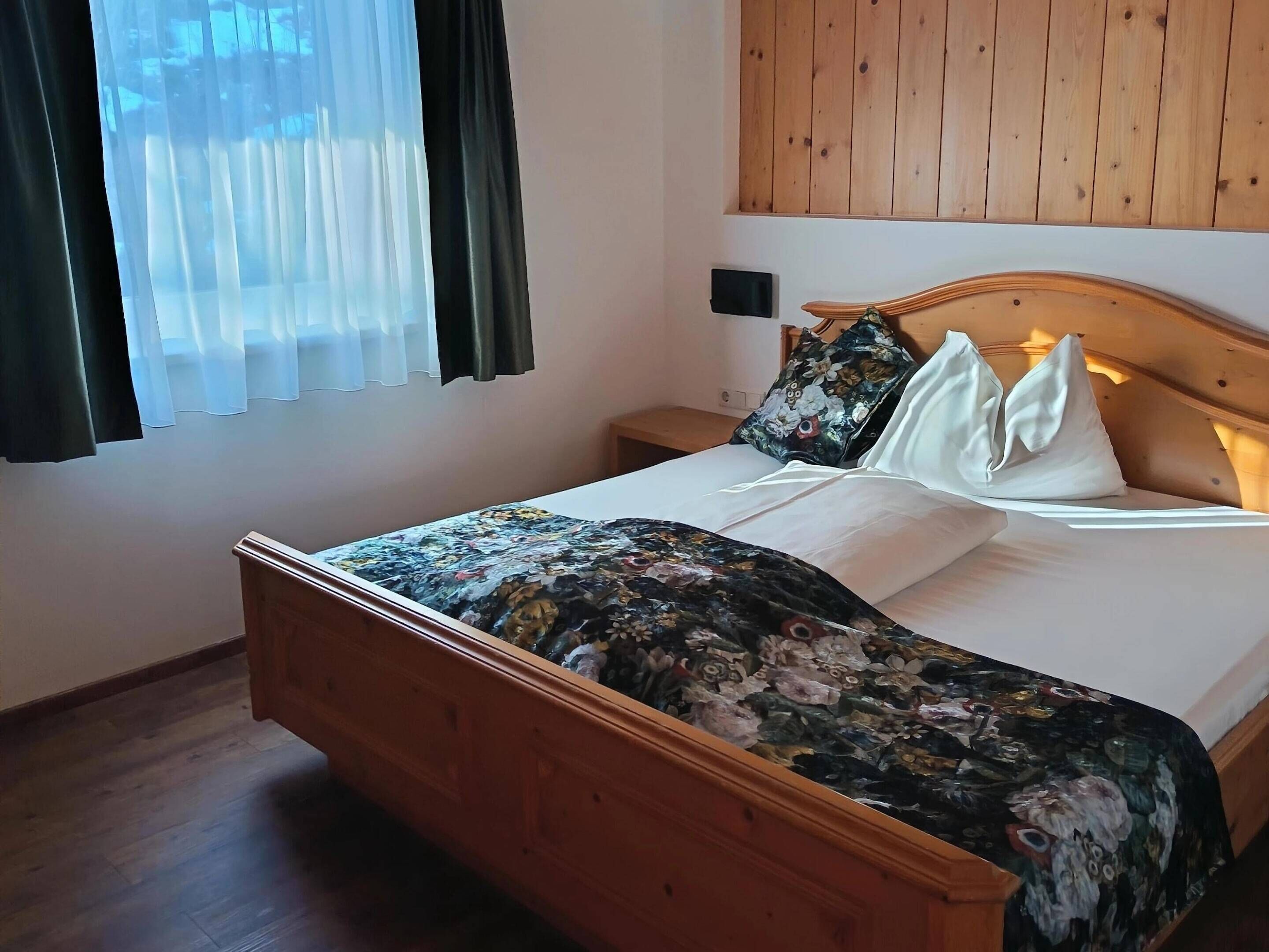 Een net opgemaakt bed met bloemenbedrukking, een houten hoofdbord en een nachtkastje met een lamp.