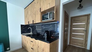 A compact kitchen with wooden cabinets, a black countertop, a sink, a microwave, and a coffee maker. - Apartment for 5 People Near the sea in Grzybowo (Kolobrzeg)