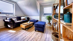 Un soggiorno in stile loft con soffitto a falda, pavimento in legno, un divano blu scuro, un poggiapiedi e un tavolino da caffè in legno, e una libreria con diversi oggetti.
