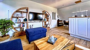 Un soggiorno moderno con un’ampia televisione a schermo piatto, scaffali in legno, un divano blu e un tavolino da caffè in legno.