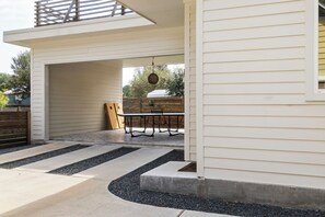 Un patio couvert avec une table et des chaises, un banc en bois et un chemin en béton.
